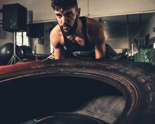 Homme soulevant un pneu de tracteur, pour exercer le cours de cross training prévu tous les vendredi à la salle de sport FITNESS MORTEAU